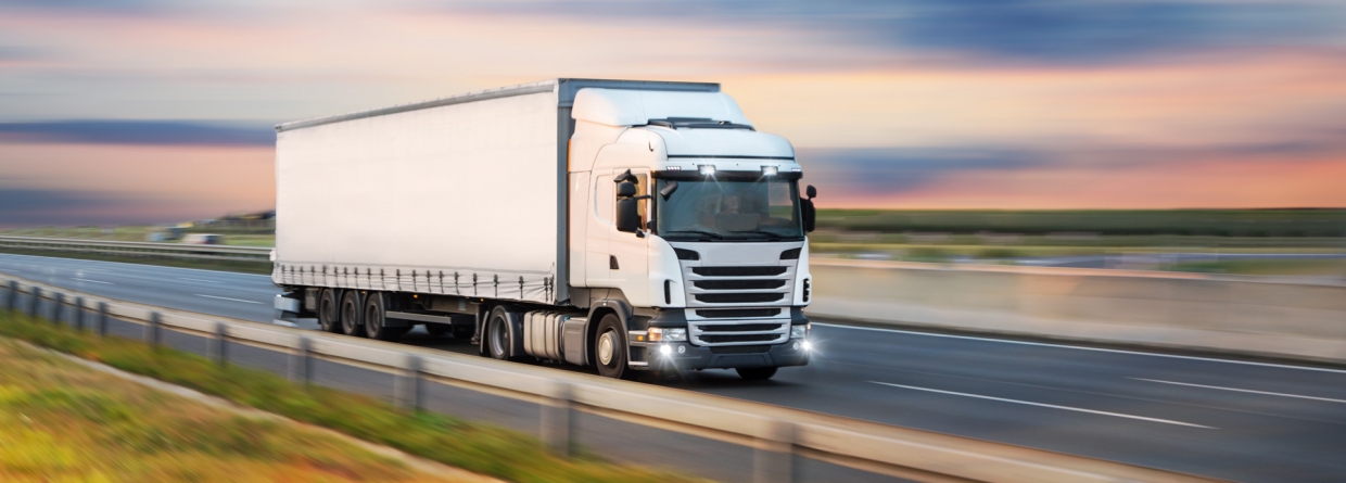Een witte vrachtwagen onderweg op de grote weg bij ondergaande zon