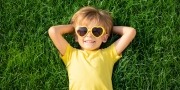 Jongetje met een geel t-shirt en gele zonnebril ligt lekker ontspannen in het gras